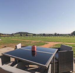 A patio table with chairs overlooking a fenced grassy field at Leadon View Oak in Upleadon near Newent