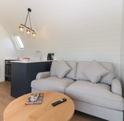 A small living area with a grey sofa, wooden round table, kitchen counter with sink and kettle at Leadon View Oak in Upleadon near Newent