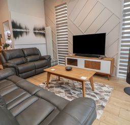 A living room with grey leather sofas a wooden coffee table a television on a stand and a wood stove at The Lodge @ Racecourse House in Babell near Holywell