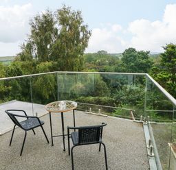 A balcony with two black chairs and a small round table overlooking green trees at Rushfield in St Dogmaels North Pembrokeshire