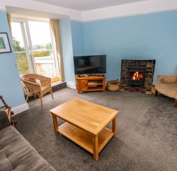 A living room with a wooden coffee table a TV on a wooden stand a fireplace and seating at Rushfield in St Dogmaels North Pembrokeshire