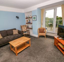 A living room with a sofa coffee table rocking chair wicker chair television and a balcony door at Rushfield in St Dogmaels North Pembrokeshire