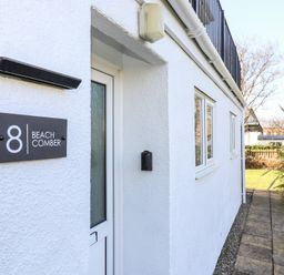 The exterior entrance of a white building with a black sign reading 8 Beachcomber and a walkway beside it at Beachcomber Maer near Bude