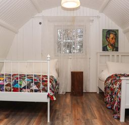A bedroom with two white beds with colorful quilts a small wooden table a window with sheer curtains and a portrait painting on the wall at Ballybeg Pod 9 Ballybeg near Tinahely County Wicklow