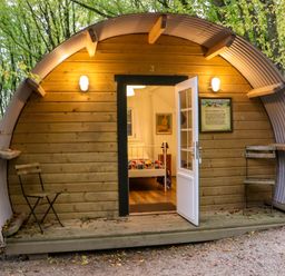 A wooden pod with curved metal roof and open door showing a bed inside with two folding chairs outside at Ballybeg Pod 4 Ballybeg near Tinahely County Wicklow