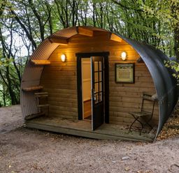 A wooden pod with curved metal roof in a forest with a door open and two metal chairs outside at Ballybeg Pod 7 Ballybeg near Tinahely County Wicklow