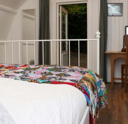 A bedroom with a white metal bed frame with a colorful quilt a wooden desk and chair and an open door leading outside at Ballybeg Pod 7 Ballybeg near Tinahely County Wicklow
