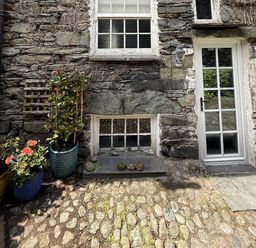 An exterior view showing a stone wall with a door and plants at Unicorn Cottage in Ambleside