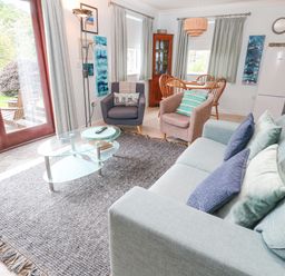 A living room with sofa armchairs glass coffee table and dining table at Chy Lowena in Goldenbank near Budock Water