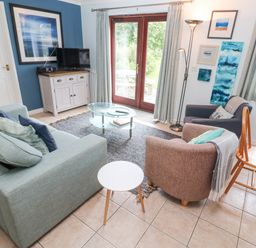 A living room with blue and brown chairs a glass coffee table and a cabinet with a television at Chy Lowena Goldenbank near Budock Water