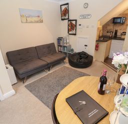 A living room with a gray sofa a round wooden table a black bean bag and a kitchenette at 5 Lyonesse Apartments in St Ives