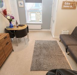 A living room with gray sofa dining table chairs and a wooden cabinet at 5 Lyonesse Apartments in St Ives