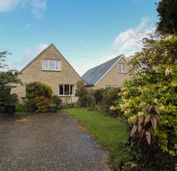 A gravel driveway with shrubs and two stone houses in the background at Old Harry Cottage 16 in Swanage