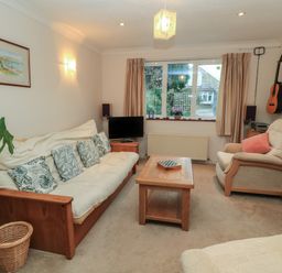 A living room with a couch, armchair, coffee table, TV, bookshelf, and guitar on the wall at Old Harry Cottage 16 Swanage