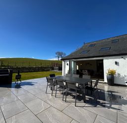 An outdoor patio with a dining table and chairs next to a white building with skylights at Beudy Pwll Pridd in Llangollen