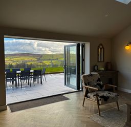 A living room with a patterned armchair a desk lamp and an outdoor dining table on a tiled patio at Beudy Pwll Pridd in Llangollen