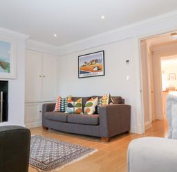 A living room with a gray sofa with patterned cushions a fireplace and a framed picture above the sofa at 6 Willows Green in Aldeburgh