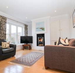 A living room with a black armchair brown sofa a television on a wooden stand a fireplace and patterned curtains at 6 Willows Green in Aldeburgh