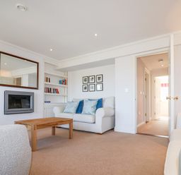 A living room with a wooden coffee table two white sofas wall-mounted fireplace bookshelves and framed pictures at 6 Willows Green in Aldeburgh