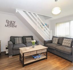 A living room with two grey sofas a wooden coffee table with flowers and board games under the stairs at 102 Waterside Park Corton