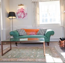 A living room with a green sofa two pillows a glass coffee table rug and a painting at Holm Oak Lodge in Tendring near Weeley