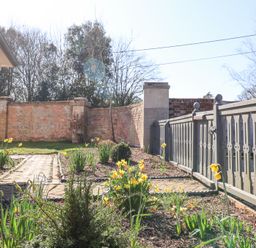 A garden with yellow flowers and a paved pathway next to a house and a wooden fence at Holm Oak Lodge in Tendring near Weeley