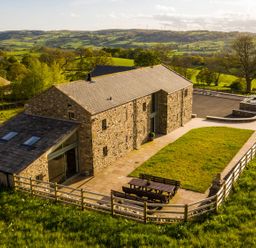 A stone barn with a fenced yard and outdoor seating table in a rural landscape at High View Barn in Sedbergh