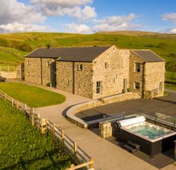 A stone barn with patio furniture and a hot tub in a rural area at High View Barn in Sedbergh