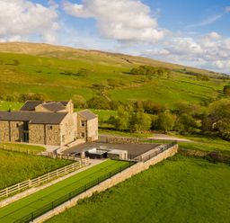 A stone barn with a hot tub and fenced outdoor area on green fields at High View Barn in Sedbergh
