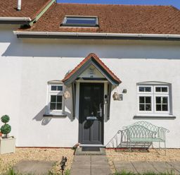 The exterior of a house with a black door two windows a small garden bench and a potted plant at The Cwtch in Aberporth