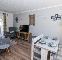 A living room and dining area with grey armchair and sofa a wooden TV cabinet and a dining table set with plates at The Cwtch in Aberporth