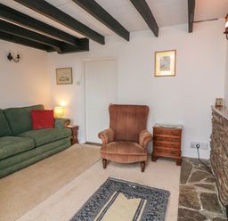 A living room with a green sofa red cushions a brown armchair wooden side tables and a stone fireplace at Vine Cottage in East Prawle