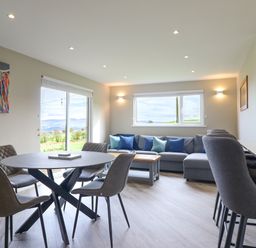 A dining area with a round table and four chairs next to a living area with a sectional sofa and a coffee table at Orchard Lodge in Maerdy near Corwen