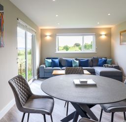 A dining area with a round table and four chairs next to a living room with a sofa and colorful cushions at Orchard Lodge in Maerdy near Corwen