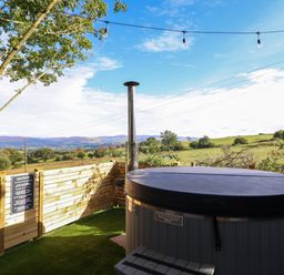 An outdoor area with a covered hot tub next to a wooden fence and a tree with string lights above at Orchard Lodge Maerdy near Corwen