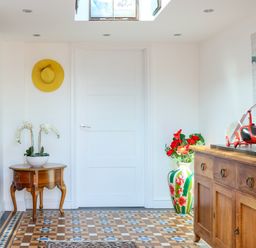 An entryway with a wooden table holding a plant a yellow hat on the wall a large floral vase with red flowers a wooden cabinet with a red helicopter model and a world map on the wall at Howard Cottage North Littleton near Offenham