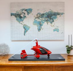 A wooden table with a red model helicopter a decorative silver object and a potted orchid below a world map on the wall at Howard Cottage in North Littleton near Offenham