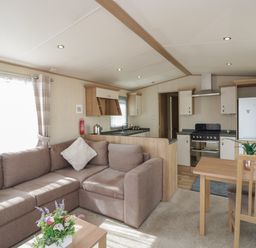 An open living room and kitchen area with a brown sofa, a wooden dining table, and kitchen appliances at Elm in Denny