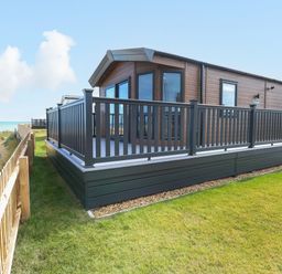 An exterior view of a wooden lodge with a glass railing deck and grass surrounding the property at Seaview Lodge in Bacton