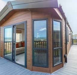 Exterior view of a wooden lodge with large windows and a deck with railing at Seaview Lodge in Bacton
