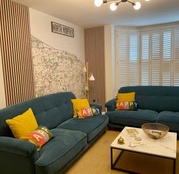 A living room with two blue sofas with colorful and yellow cushions a marble coffee table and a large map on the wall at Happy Place in Sheringham