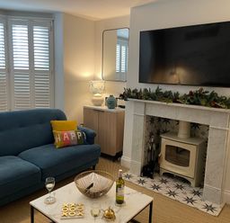 A living room with a blue sofa and colorful pillows a coffee table with wine glasses and a tic tac toe game a fireplace with greenery and a TV mounted above at Happy Place in Sheringham