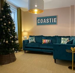 A living room with a decorated Christmas tree blue sofa and a lamp at Happy Place in Sheringham