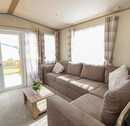 A living room with a brown sectional sofa, a wooden coffee table with flowers, plaid curtains, and glass doors at Hazel in Denny