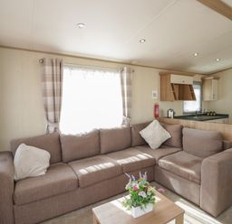 A living room with a beige sectional sofa pillows and a floral arrangement on a wooden coffee table at Hazel in Denny