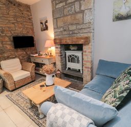A living room with a blue sofa with patterned cushions a wicker armchair a wooden coffee table and a stone fireplace at The Coquet Nest in Rothbury