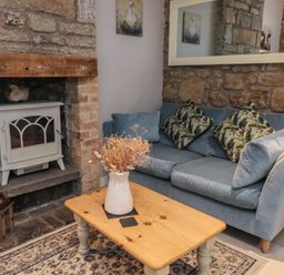 A living room with a blue sofa a wooden coffee table with a vase and fireplace at The Coquet Nest in Rothbury