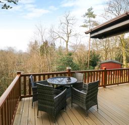 An outdoor deck with a round glass table and four wicker chairs surrounded by trees at Esk Pike 9 Skiptory Howe White Cross Bay near Windermere