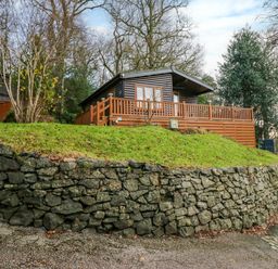 A wooden cabin on a grassy hill behind a stone wall surrounded by trees at Esk Pike 9 Skiptory Howe White Cross Bay near Windermere
