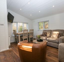 A living room with a dining table and chairs a sofa an armchair a round coffee table and a mounted television at Esk Pike 9 Skiptory Howe White Cross Bay near Windermere